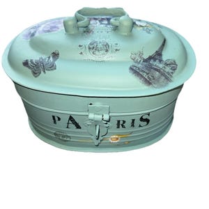 May include: A mint green metal storage box with a lid and handle. The lid features a butterfly and Eiffel Tower design. The word "PARIS" is printed on the front. The box has a clasp closure.