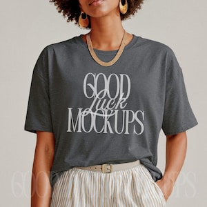 May include: A dark gray t-shirt with the text "GOOD luck MOCKUPS" in white. The model is wearing striped shorts with a light-colored belt and gold jewelry.