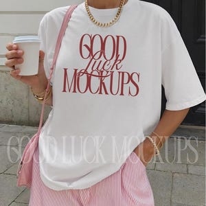 May include: White t-shirt with the text "GOOD LUCK MOCKUPS" in red, paired with pink and white striped shorts. The outfit is accessorized with gold jewelry and a pink purse.
