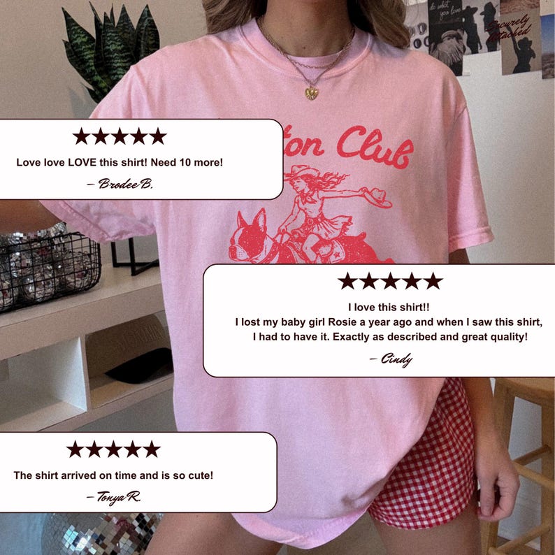 May include: A light pink t-shirt featuring a red graphic print of a person wearing a cowboy hat riding a dog, with the text "on Club" visible above the graphic. The shirt has a crew neckline and short sleeves, worn with red and white checkered shorts.