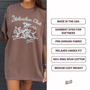 Puede incluir: Una camiseta marr&oacute;n con un gr&aacute;fico azul claro de una persona montando un chihuahua con el texto The Chihuahua Club y Fearless by Nature. Los cuadros de texto enumeran: Made in the USA, Garment Dyed for Softness, Pre-Shrunk Fabric, Relaxed Unisex Fit, 100% Ring Spun Cotton, Medium Cozy Weight.