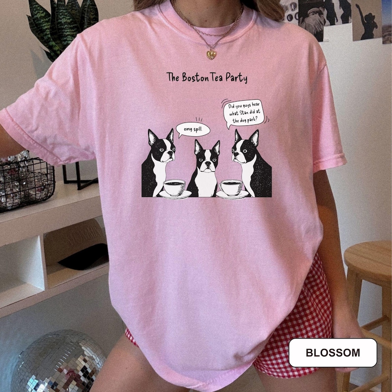 May include: A light pink t-shirt with a graphic of three Boston Terriers at a tea party. The dogs are black and white, with speech bubbles that say "omg spill" and "Did you guys hear what Stan did at the dog park?" The text "The Boston Tea Party" is above the graphic.