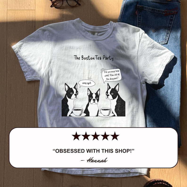 May include: White t-shirt featuring a Boston Terrier-themed design. The shirt displays the text "The Boston Tea Party" and a cartoon of three Boston Terriers with teacups. Speech bubbles read "omg spill" and "Did you guys hear what Stan did at the dog park?"