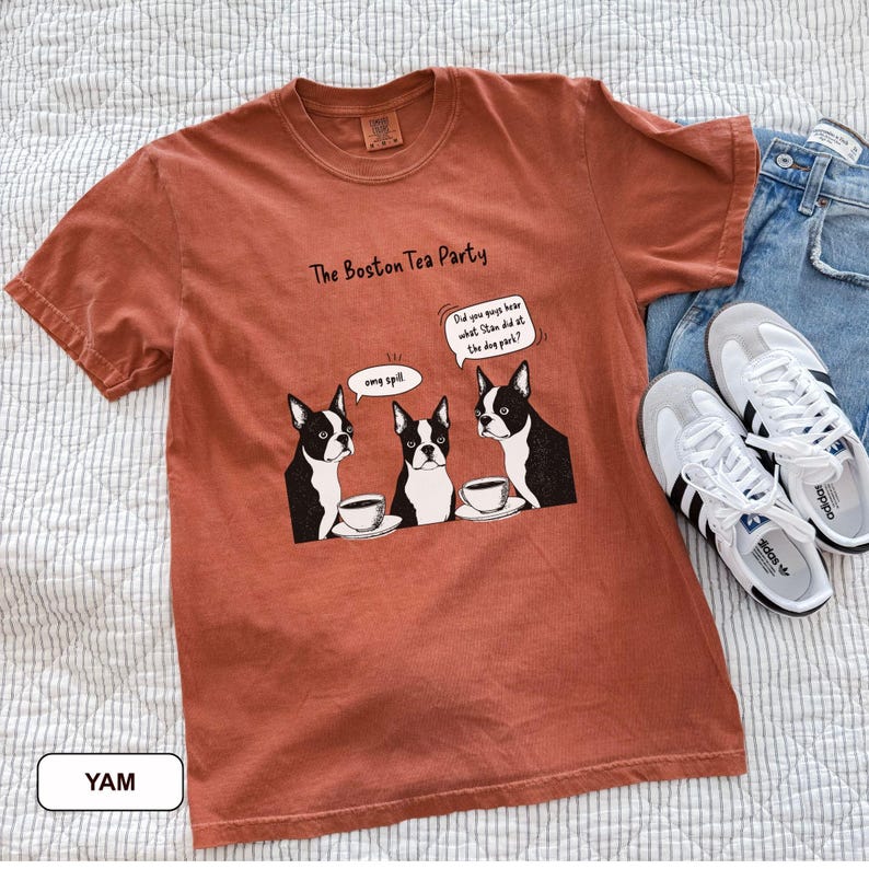 May include: A rust-colored t-shirt with the text "The Boston Tea Party" and a cartoon of three Boston Terriers with teacups. The dogs are in a conversation bubble that says "Did you guys hear what Stan did at the dog park?"