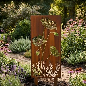 May include: A rectangular, rusty-brown metal garden art piece with a poppy flower design. The poppy flowers and foliage are cut out, creating a silhouette effect. The art piece is set in a garden with various plants and flowers.