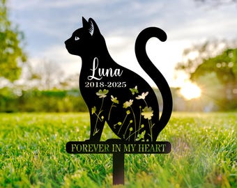 May include: Black metal cat silhouette garden stake with the name "Luna" and dates "2018-2025". The cat design features cut-out flowers and butterflies, with the words "FOREVER IN MY HEART" at the base. The stake is placed in green grass.