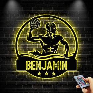 Può includere: Un'opera d'arte da parete illuminata in nero e giallo con una silhouette di giocatore di pallanuoto. Il nome "BENJAMIN" è visualizzato sotto la figura, con tre stelle. L'opera d'arte è ambientata su uno sfondo di muro di mattoni.