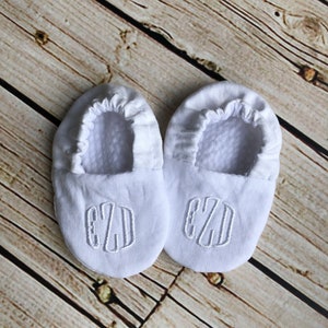 White crib shoes on wood background.  Crib shoes are monogramed in white rounded font - EZD.