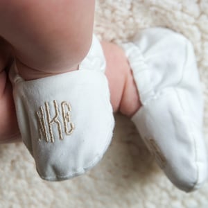 Monogrammed Infant Baptism Crib Shoes. White crib shoes on baby feet.  Monogramed in champagne gold, rounded font - nKE