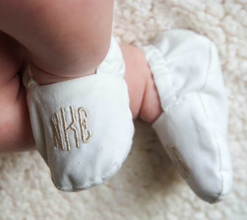 Monogrammed Infant Baptism Crib Shoes. White crib shoes on baby feet.  Monogramed in champagne gold, rounded font - nKE