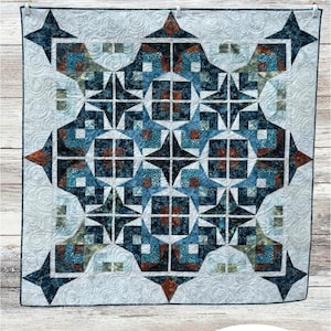May include: A quilted wall hanging with a geometric starburst pattern in shades of blue, teal, and rust. The quilt features the text "Perfect Rhythm" and is signed by Amanda Bauer. The background is a light cream color with a cat illustration.