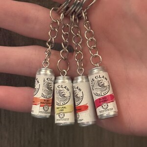 Puede incluir: Llaveros de mini latas de White Claw hard seltzer. Cada llavero presenta un sabor diferente: Ruby Grapefruit, Natural Lime, Berry y Black Cherry. Las latas est&aacute;n unidas a una cadena y un llavero plateados.