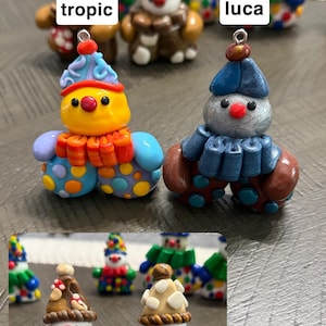 May include: A collection of small, colourful clown figurines with metal loops for hanging. The figures feature distinct designs labelled as tropic, luca, mushy, and chocho, showcasing various hats, ruffled collars, and polka-dot patterns in vibrant colours.