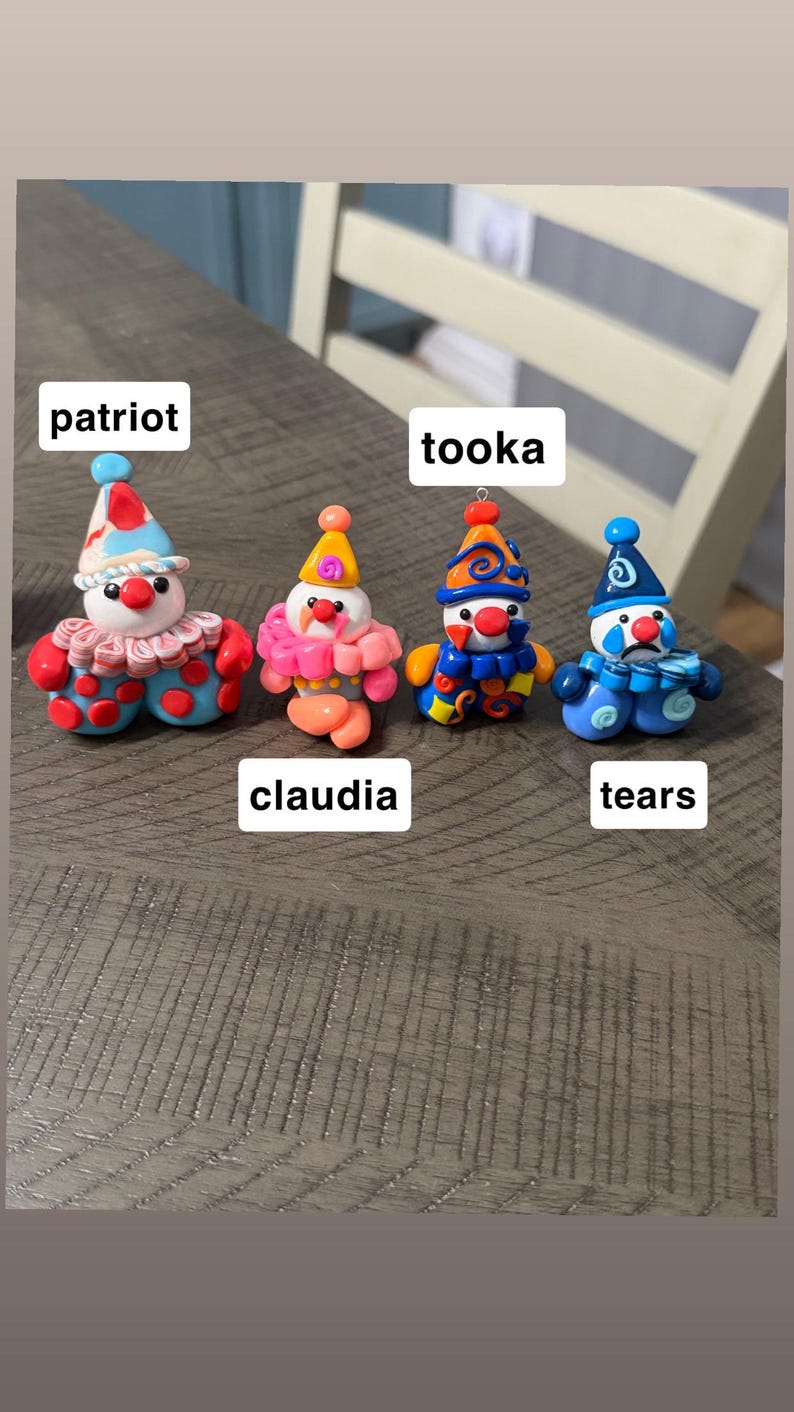 May include: Four small clown figurines made of clay. The first, labelled patriot, has a red, white, and blue hat and outfit. The second, claudia, is pink and orange. The third, tooka, is blue and orange. The fourth, tears, is blue with a sad face.