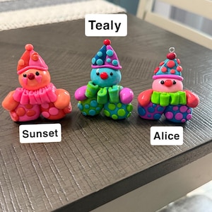 May include: Three small clown figurines labelled Sunset, Tealy, and Alice. Sunset is orange and pink with polka dots. Tealy is blue, green, and purple with polka dots. Alice is pink, blue, and green with polka dots and a small metal loop on top.