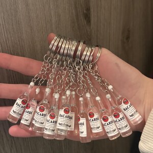 Puede incluir: Una colecci&oacute;n de llaveros de botellas de Bacardi en miniatura. Cada botella de pl&aacute;stico transparente tiene una etiqueta blanca con texto rojo y negro. Los llaveros est&aacute;n unidos a anillos de metal plateado.