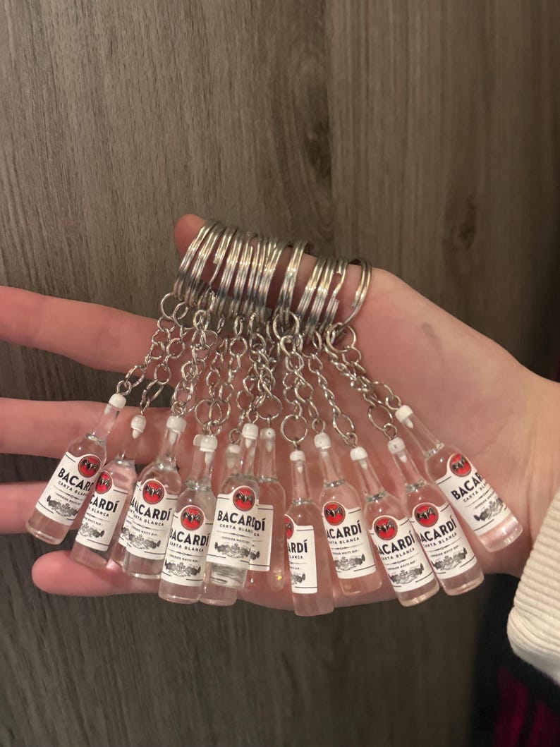 Puede incluir: Una colecci&oacute;n de llaveros de botellas de Bacardi en miniatura. Cada botella de pl&aacute;stico transparente tiene una etiqueta blanca con texto rojo y negro. Los llaveros est&aacute;n unidos a anillos de metal plateado.