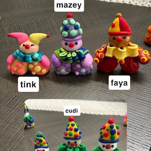 May include: Six small, colourful clay clown figurines labelled with names. Top row: Tink, Mazey, and Faya. Bottom row: Doucey, Cudi, and Scooter. Each clown features a unique hat, ruffled collar, and polka-dot pattern in vibrant shades of red, yellow, blue, green, and purple.