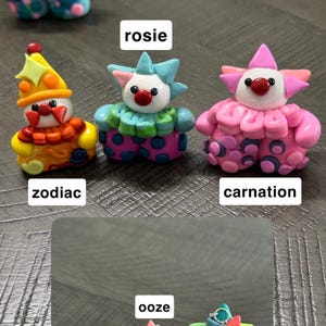 May include: A collection of six small, colourful clown figurines crafted from clay. Each figure features a unique colour scheme, including zodiac, rosie, carnation, dottie, ooze, and laffy, with distinct hats, ruffled collars, and polka-dot patterned trousers.