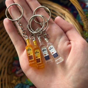 Puede incluir: Llaveros de botellas de tequila en miniatura. Dos botellas de color &aacute;mbar y dos botellas transparentes con el logo "Cuervo". Cada llavero tiene un anillo y una cadena plateados.