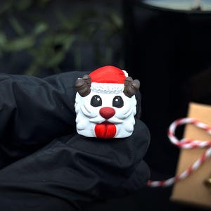 May include: A festive figurine of Santa Claus in white, red, and brown, with a red hat and tongue. The figurine has black eyes and brown antlers. The text "REAL PHOTO - NO RENDERS" is at the bottom of the image.