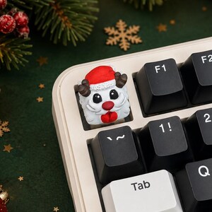 Könnte beinhalten: Eine individuelle Artisan-Tastenkappe in Form eines weißen Wesens mit roter Nase, roter Weihnachtsmannmütze und braunem Geweih, montiert auf einer mechanischen Tastatur mit schwarzen und weißen Tasten und standardmäßiger Beschriftung.