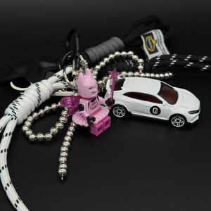 Pode incluir: Um porta-chaves com uma minifigura de Batman fada rosa com asas translúcidas e uma varinha de estrela, preso a um cordão de paraquedas branco e preto, uma corrente de bolas prateada e um carro de brinquedo branco com um logótipo preto.