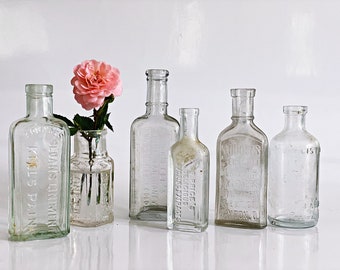 6 Vintage apothecary bottles. An embossed, salvaged glass quack cure medicine bottle collection. Repurposed bud vases for shelf display.