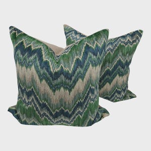 May include: Two decorative throw pillows with a green, blue, and beige zigzag pattern. The pillows have a textured appearance and a neutral-colored backing. The design is reminiscent of a chevron pattern, adding a modern touch to home decor.