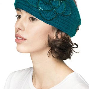 K&ouml;nnte beinhalten: T&uuml;rkisfarbenes Strickstirnband mit einer gro&szlig;en, dekorativen Blume. Die Blume ist mit Pailletten und Perlen verziert. Das Stirnband hat eine einfarbige t&uuml;rkisfarbene Farbe und scheint aus einem weichen, strukturierten Garn zu bestehen. Ein stilvolles Accessoire.