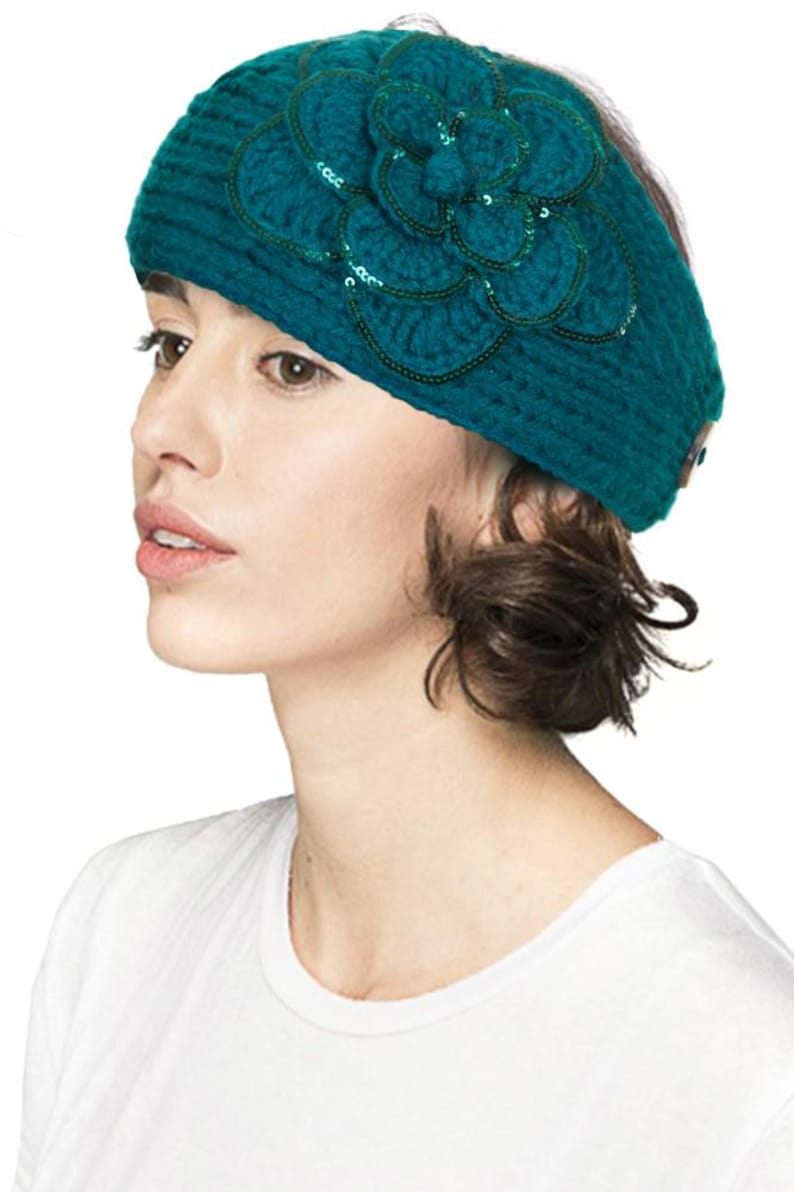 K&ouml;nnte beinhalten: T&uuml;rkisfarbenes Strickstirnband mit einer gro&szlig;en, dekorativen Blume. Die Blume ist mit Pailletten und Perlen verziert. Das Stirnband hat eine einfarbige t&uuml;rkisfarbene Farbe und scheint aus einem weichen, strukturierten Garn zu bestehen. Ein stilvolles Accessoire.