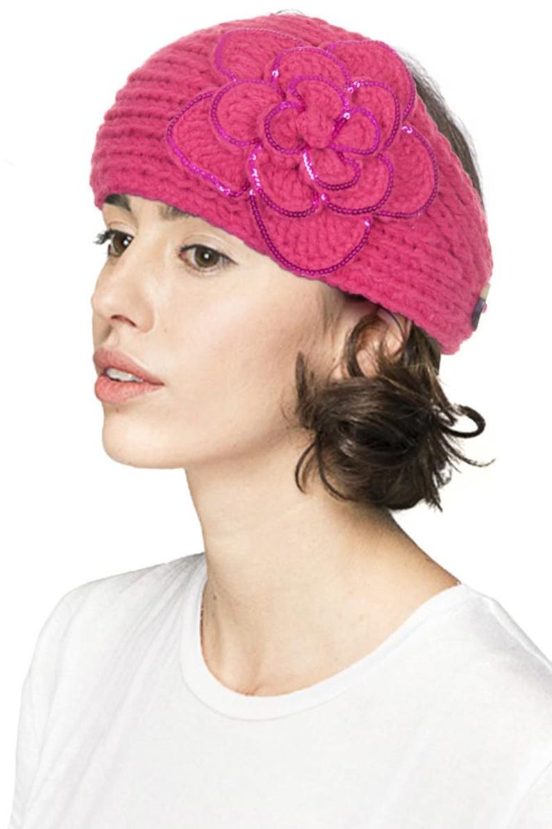 K&ouml;nnte beinhalten: Ein magentafarbenes Strickstirnband mit einer gro&szlig;en, mit Pailletten besetzten Blumenapplikation. Die Blume ist mittig auf dem Stirnband angebracht und hat mehrere Bl&uuml;tenblattschichten. Das Stirnband besteht aus dickem, strukturiertem Garn.