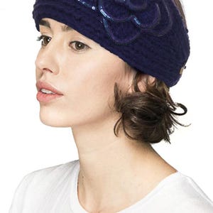 K&ouml;nnte beinhalten: Ein dunkelblaues Strickstirnband mit einer gro&szlig;en, dekorativen Blume aus dem gleichen Material. Die Blume ist mit Pailletten verziert. Das Stirnband wird von einer Person getragen, die ein wei&szlig;es T-Shirt tr&auml;gt.