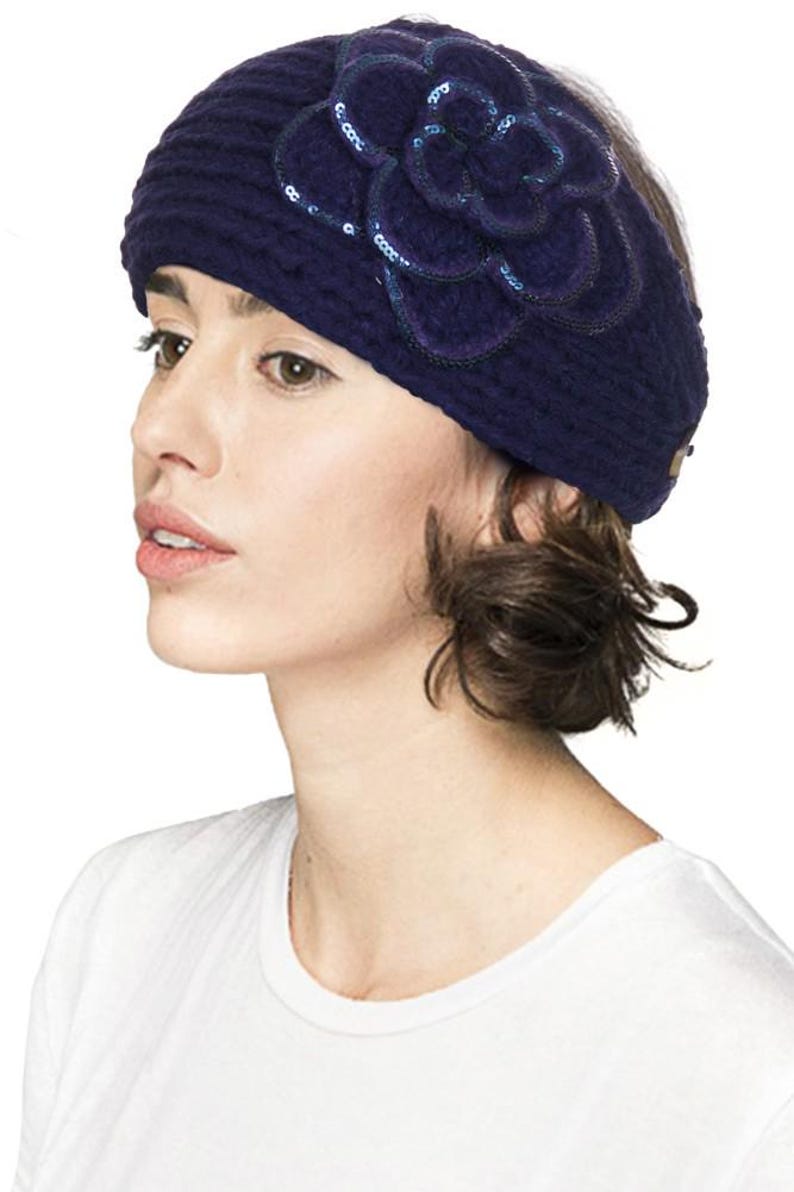 K&ouml;nnte beinhalten: Ein dunkelblaues Strickstirnband mit einer gro&szlig;en, dekorativen Blume aus dem gleichen Material. Die Blume ist mit Pailletten verziert. Das Stirnband wird von einer Person getragen, die ein wei&szlig;es T-Shirt tr&auml;gt.