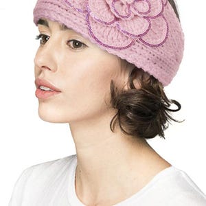 K&ouml;nnte beinhalten: Ein hellrosa gestricktes Stirnband mit einem gro&szlig;en Blumenmuster. Die Blume ist mit Pailletten verziert. Dieses Stirnband ist ein weiches, feminines Accessoire, ideal, um jedem Outfit einen Hauch von Eleganz zu verleihen.
