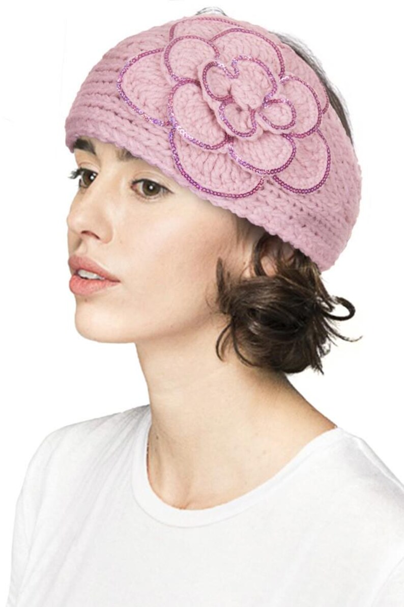 K&ouml;nnte beinhalten: Ein hellrosa gestricktes Stirnband mit einem gro&szlig;en Blumenmuster. Die Blume ist mit Pailletten verziert. Dieses Stirnband ist ein weiches, feminines Accessoire, ideal, um jedem Outfit einen Hauch von Eleganz zu verleihen.