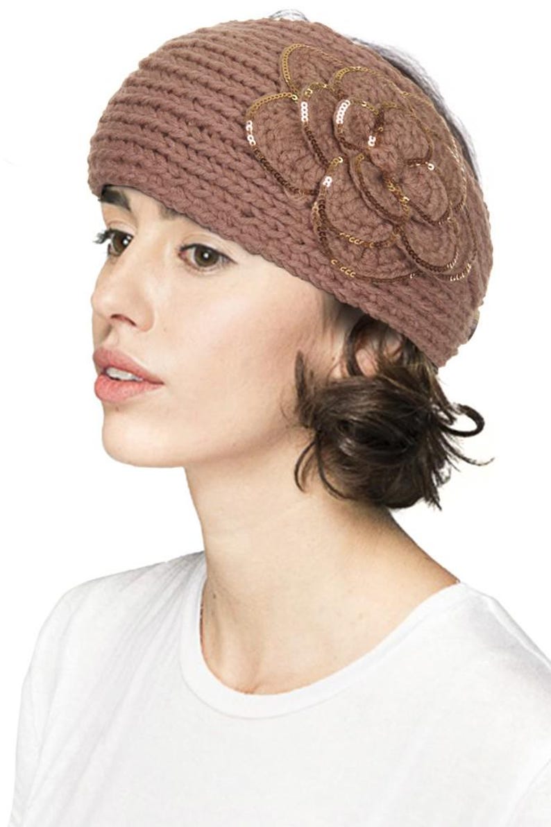 K&ouml;nnte beinhalten: Gestricktes Stirnband in ged&auml;mpftem Mauve, verziert mit einem Blumendesign mit goldenen Pailletten. Das Stirnband besteht aus dickem, strukturiertem Garn und wird auf dem Kopf getragen.