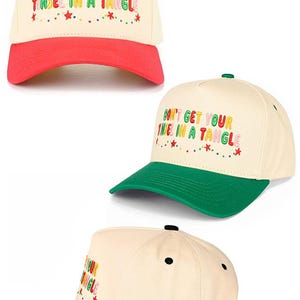May include: Cream-coloured baseball caps with the embroidered text "DON'T GET YOUR TINSEL IN A TANGLE." Each cap features a different coloured peak: red, green, and black. The caps have a festive, holiday theme.