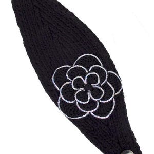 K&ouml;nnte beinhalten: Schwarzes Stirnband aus Strick mit einer gro&szlig;en, silberfarben umrandeten Blumenapplikation. Das Stirnband hat zwei dekorative Kn&ouml;pfe und den Text "Black/Silver". Ein stilvolles Accessoire.
