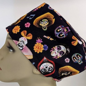 May include: Black scrub hat with a colorful print of characters and flowers from the Disney Pixar movie Coco. The print includes sugar skulls, flowers, and musical notes.