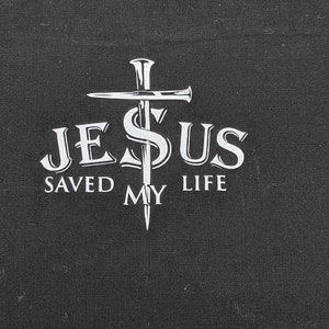 May include: White graphic on a black background of a cross with nails and the text "JESUS SAVED MY LIFE"