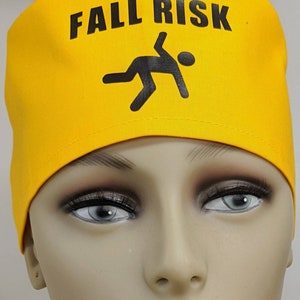 May include: Yellow surgical scrub hat with the text "FALL RISK" and a black silhouette of a person falling.