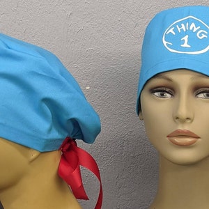 May include: A blue surgical scrub hat with a white "Thing 1" logo. The hat has red ties.
