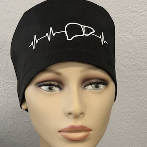 May include: Black scrub hat with a white graphic of a liver with a heartbeat line. The hat is made of a soft, comfortable fabric.