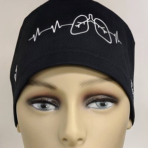 May include: Black scrub hat with a white design of a heartbeat and two lungs. The hat has the text "BT" on the left side and "BG" on the right side.