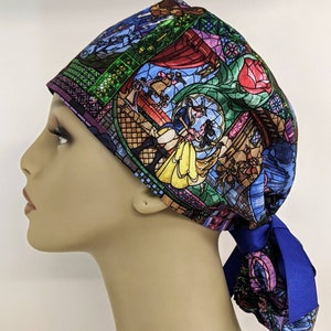 May include: A surgical scrub hat with a stained glass design featuring Belle and the Beast from Beauty and the Beast. The hat has a blue ribbon tie.