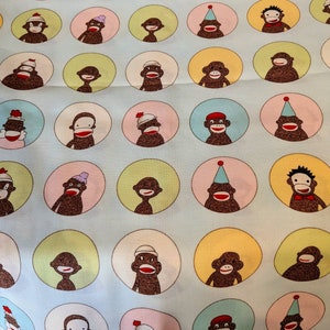 May include: A blue and white patterned fabric with a repeating design of cartoon monkeys wearing hats. The monkeys are wearing a variety of hats, including a graduation cap, a party hat, a cowboy hat, and a beanie.