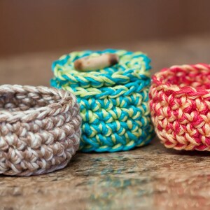 Può includere: Tre cesti in crochet di diversi colori e motivi. I cesti sono realizzati con una combinazione di filato beige, bianco, verde chiaro, turchese e rosa.