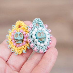 May include: Two crocheted skull charms with blue and white beads. The charm on the left has yellow crochet and pink beads. The charm on the right has green crochet and white beads.