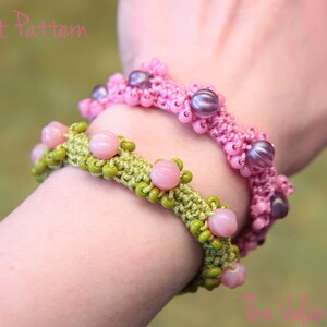 May include: Two crocheted bracelets with beads. The top bracelet is pink with purple beads. The bottom bracelet is green with pink beads. The bracelets are on a person's wrist.